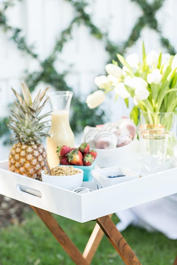 Yogurt, cocktail, flowers and a pineapple on a tray outside.