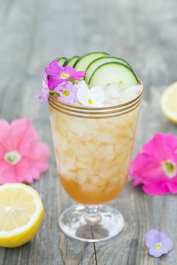 Pimm's Cup recipe in a beautiful glass with pink flowers and cucumber slices.