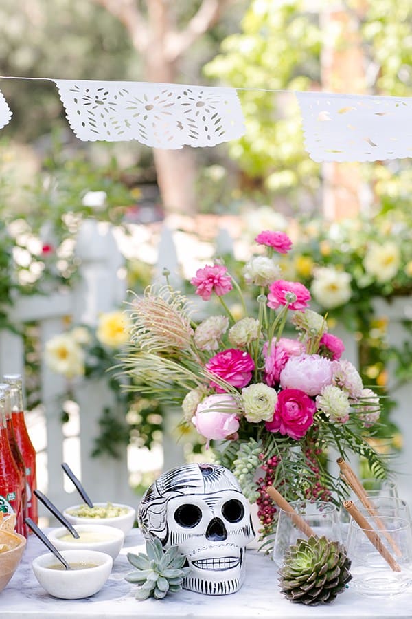 Pink flower arrangements with a black and white skull and salsa on a marble table outside for a Cinco de Mayo party.