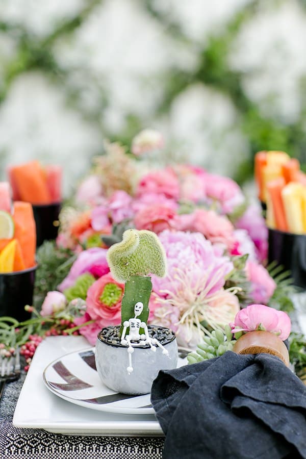 Cactus plant with a tiny skeleton and pink flowers on a black and white table for Cinco de Mayo.