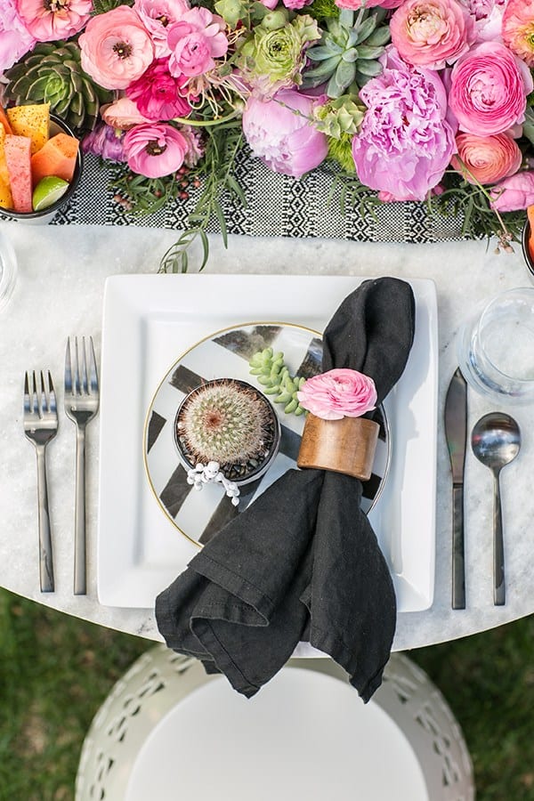 Cinco de Mayo table setting with black napkin, wooden napkin ring, pink flowers and black flatware.