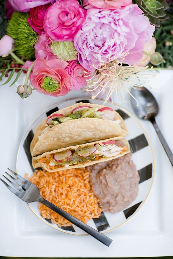 Tacos, rice and beans on a black and white plate.