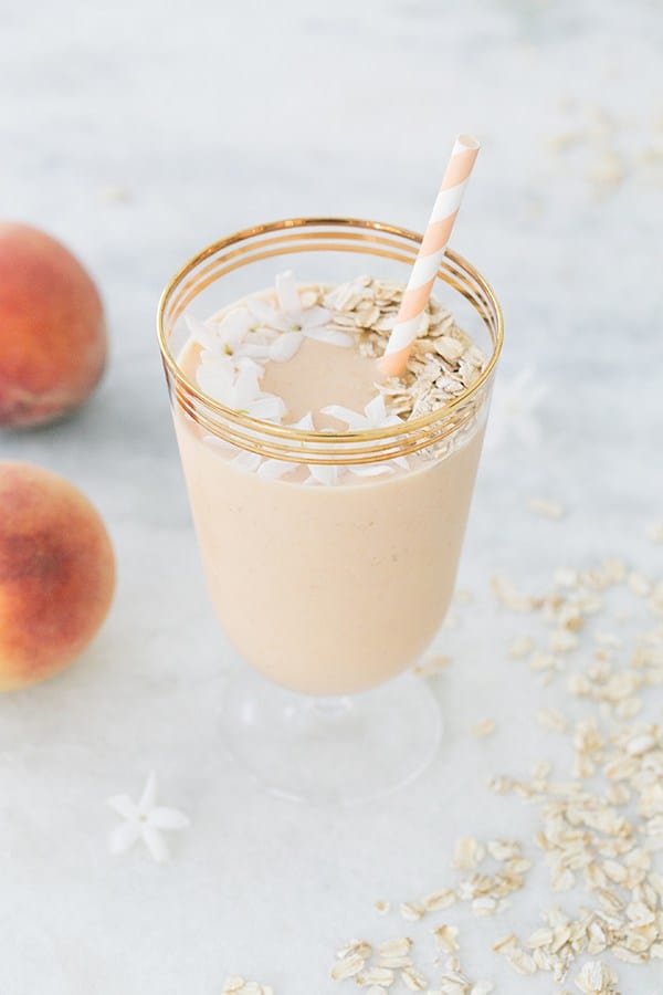 Peach smoothie with jasmine flowers, peach paper straw in gold glass.