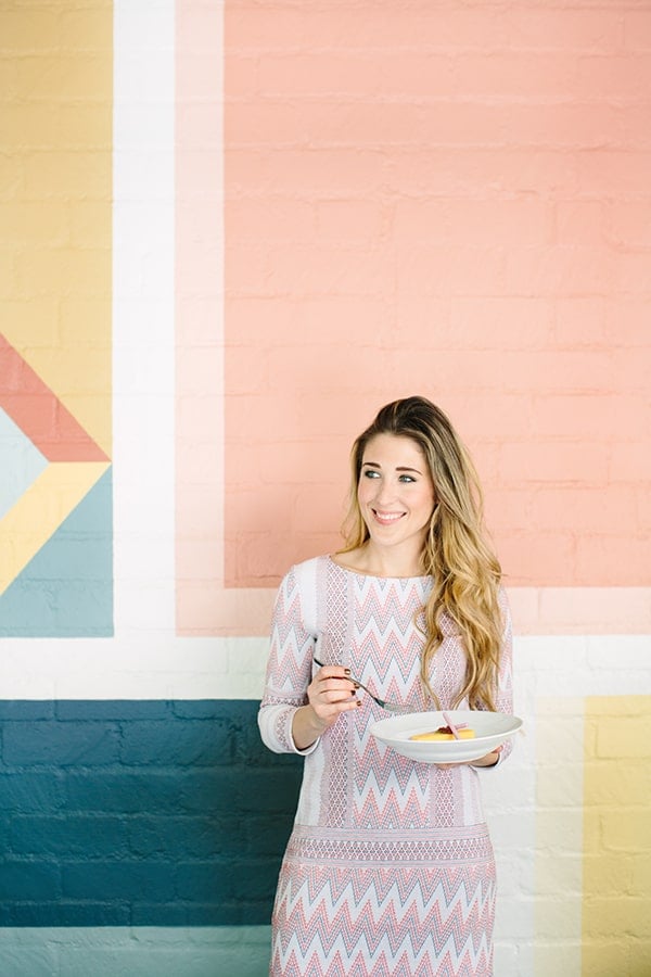 Eden Passante eating in front of colorful wall.