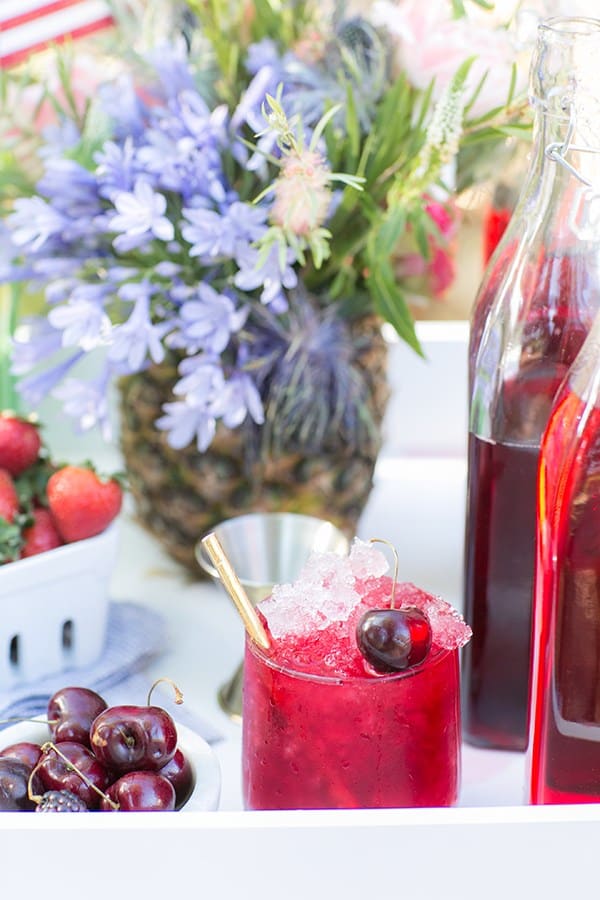 A bright red boozy snow cone with gold straws and cherry on a snow cone stand.