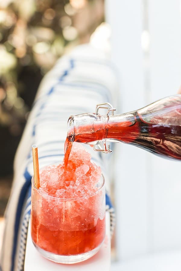 Pouring strawberry syrup into a glass filled with ice.