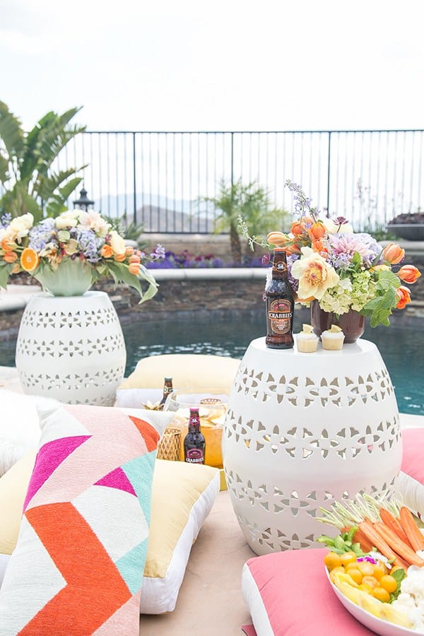 pool party ideas with pillows, flowers, drinks and garden stools.