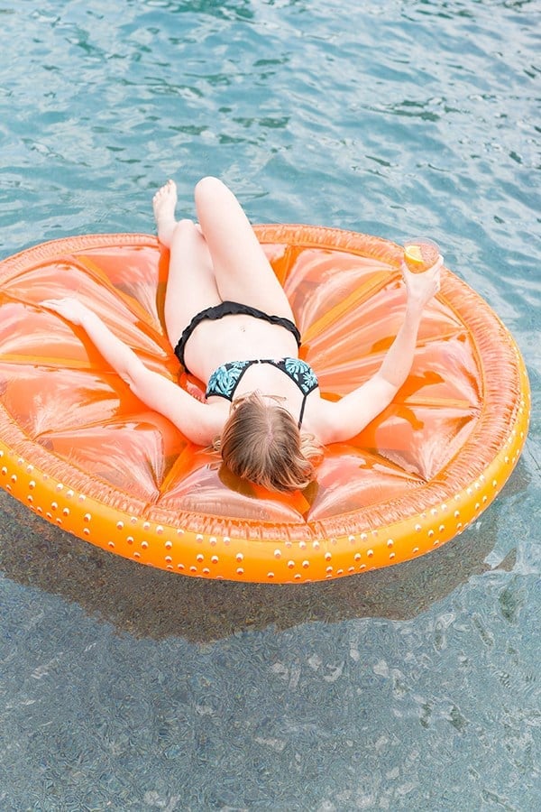 Girl in bathing suit floating on an orange slice in a pool.