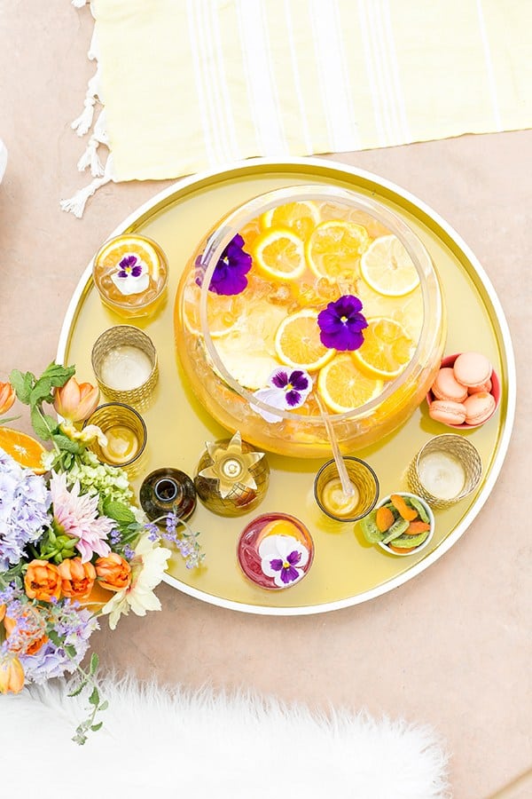 Pineapple party punch in bowl with orange slices on a yellow tray with flowers and pretty summer cups. 