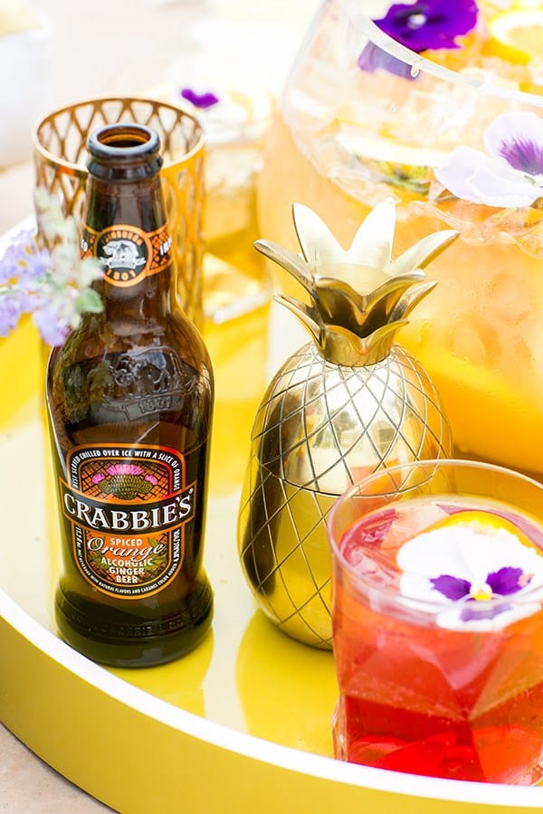 Crabbies ginger beer with a gold pineapple shaker and a cocktail on a yellow acrylic tray.