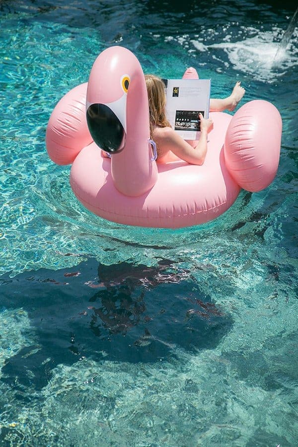 girl on a pink flamingo pool float reading a book