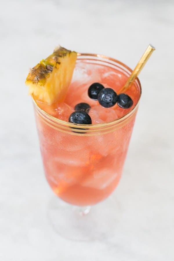 A tea cocktail with pineapple and blueberries and a gold straw.