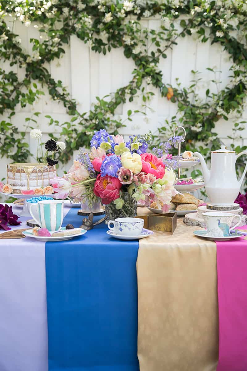 Alice in Wonderland Tea Party with colorful flowers, table linens, tea cups and desserts.