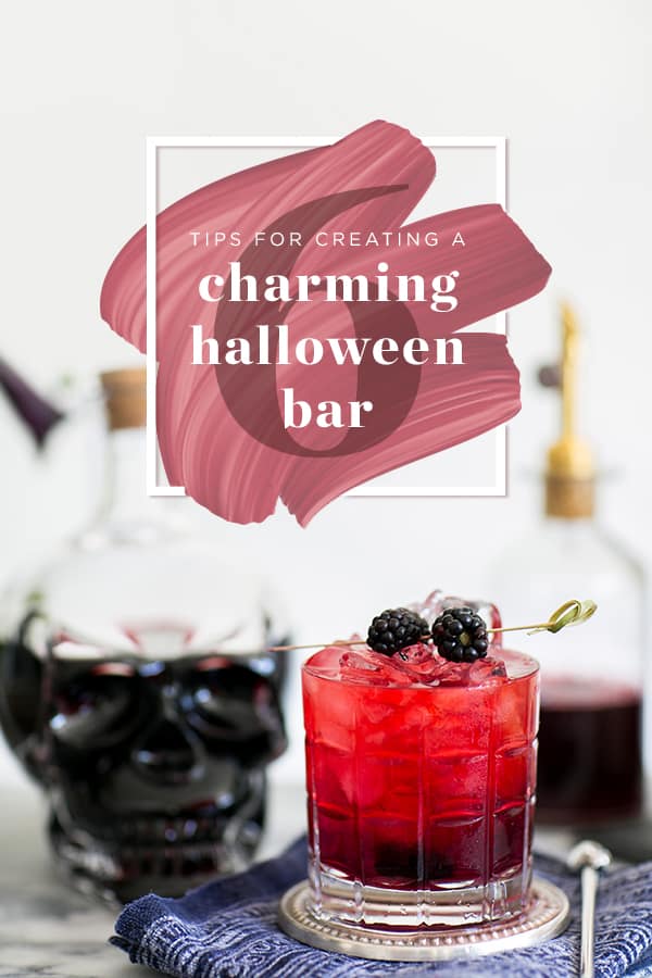 Red cocktail with blackberries and a Halloween skull.