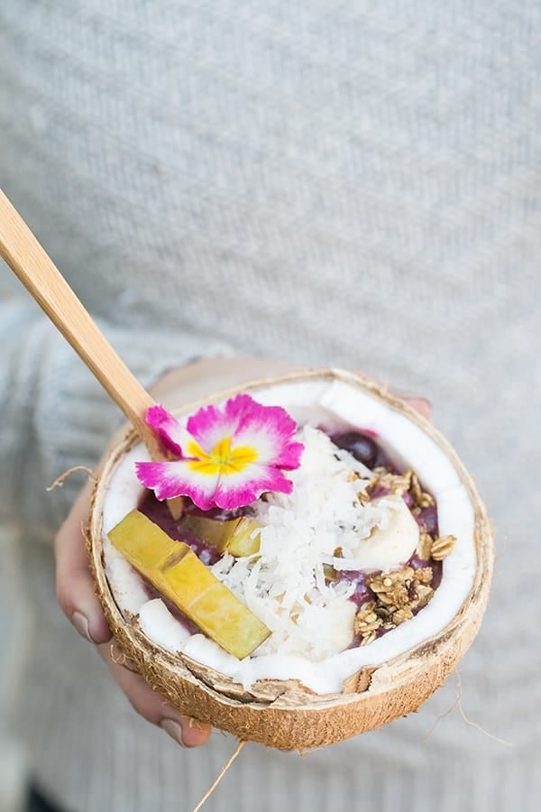 Holding an acai bowl in a coconut with shredded coconut, starfruit and an edible flower.