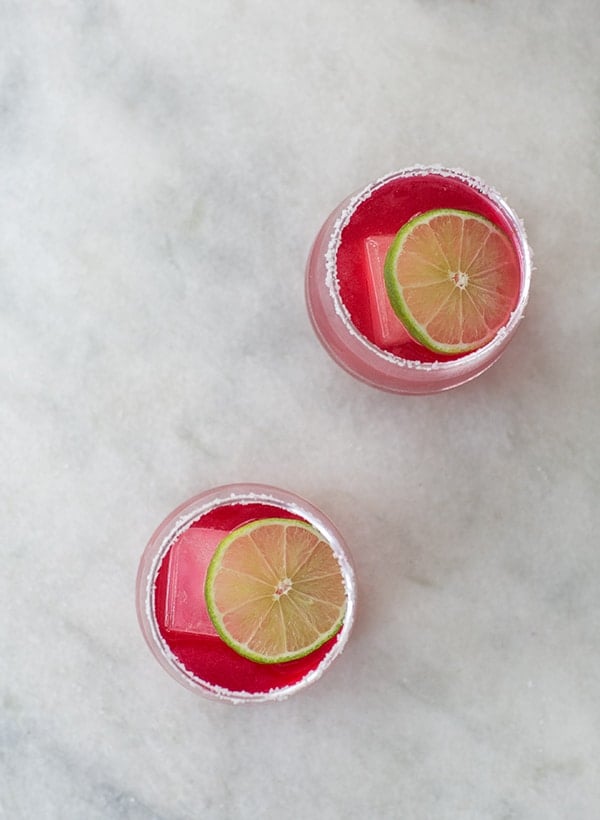 two pink hibiscus margaritas with lime slice on marble table.