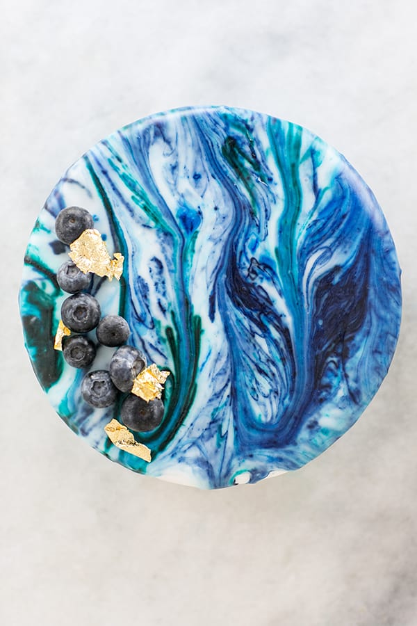 A marble drip cake decorated with blueberries and gold leaf