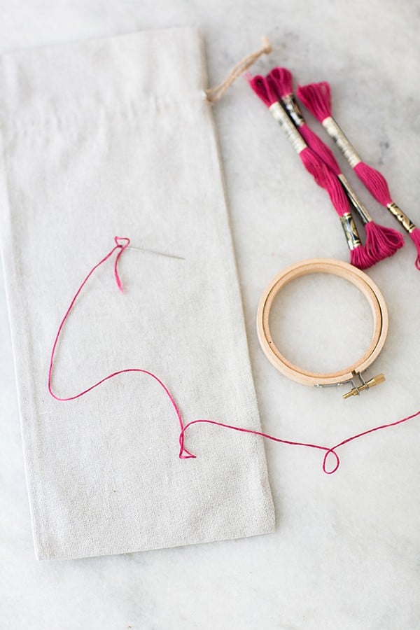 Supplies for a Valentine's Day Craft. Embroidery pin, pink yarn, wine bag on a marble table.