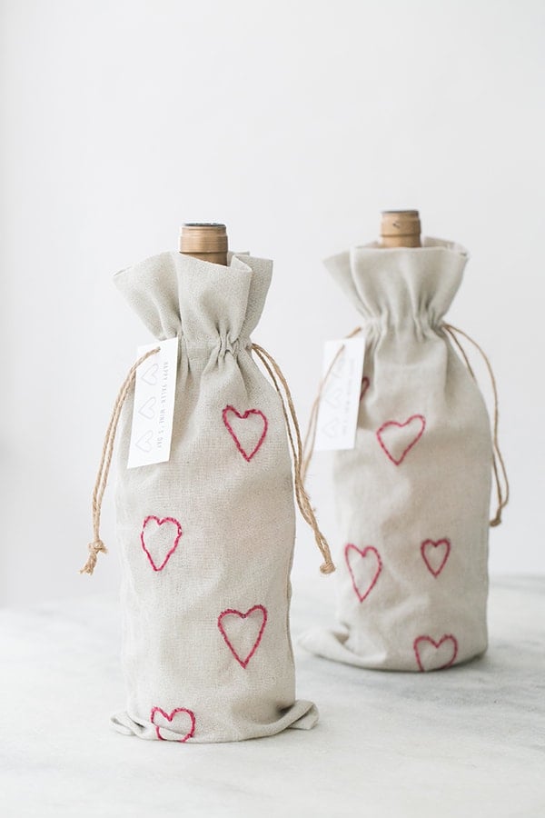 Two bottles of wine inside DIY Valentine's Day wine bags with embroidery pint hearts.