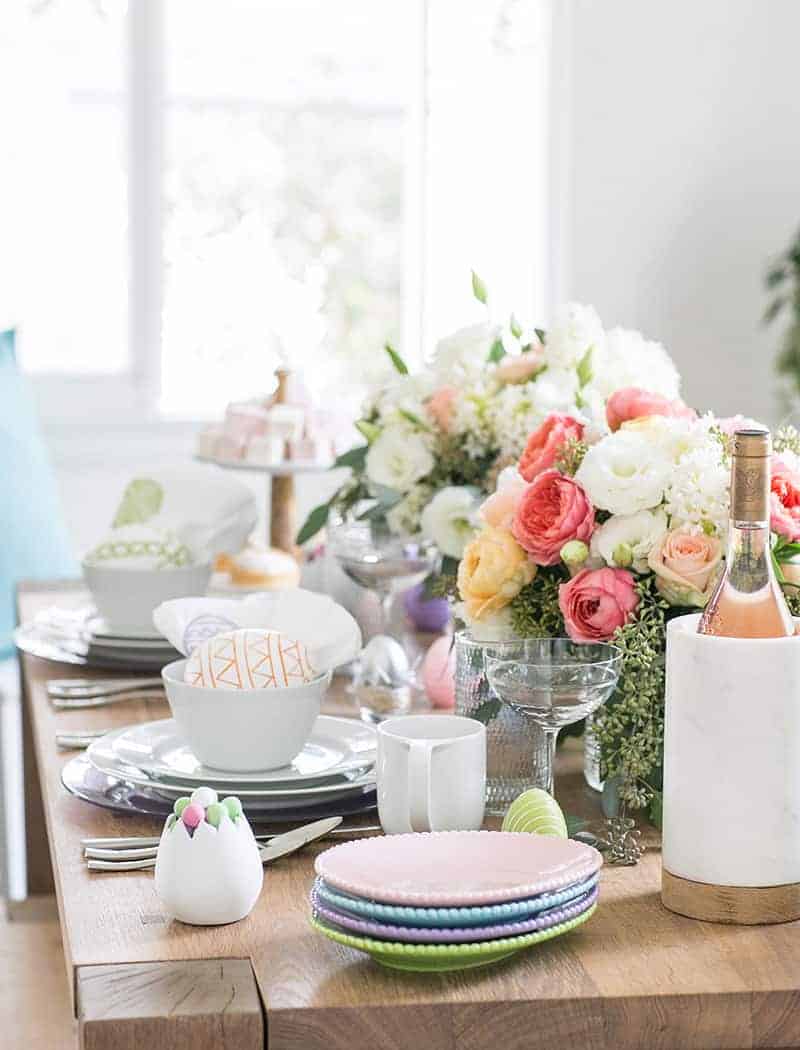 An easter table setting with flowers, wine, egg shaped plates. 