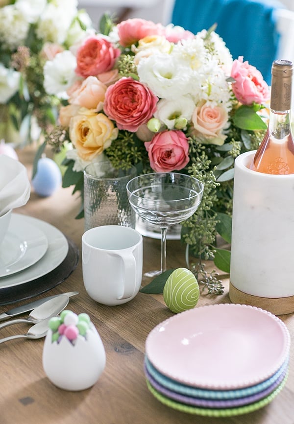 Easter brunch ideas on a table with flowers, wine, plates and candy.