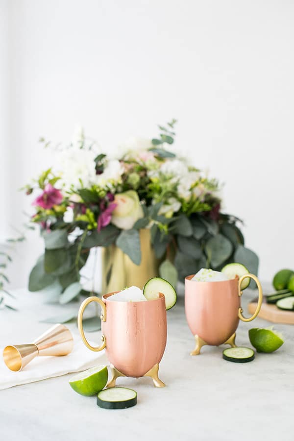 Moscow Mules in modern copper mugs on a marble table with flowers.