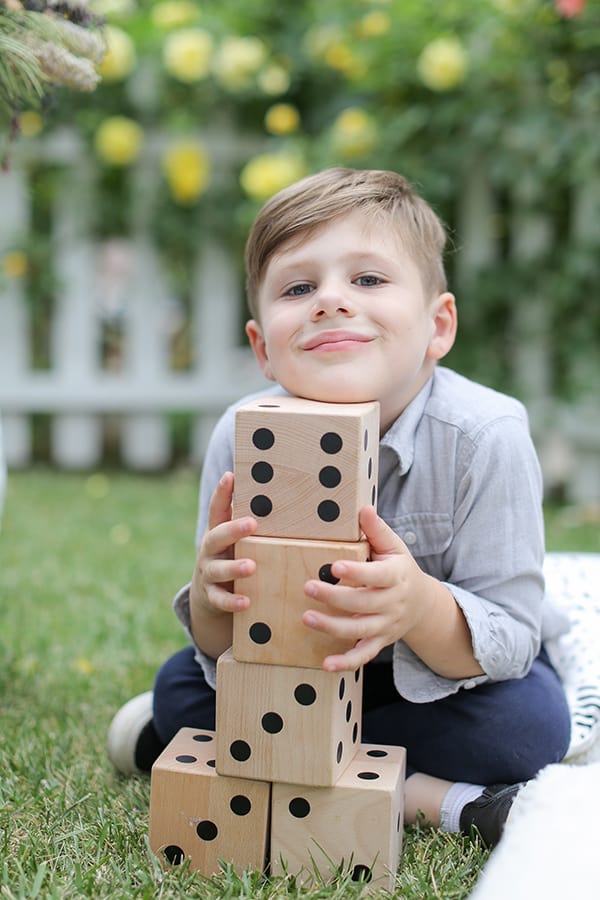 Little boy holding large dice at a picnic.