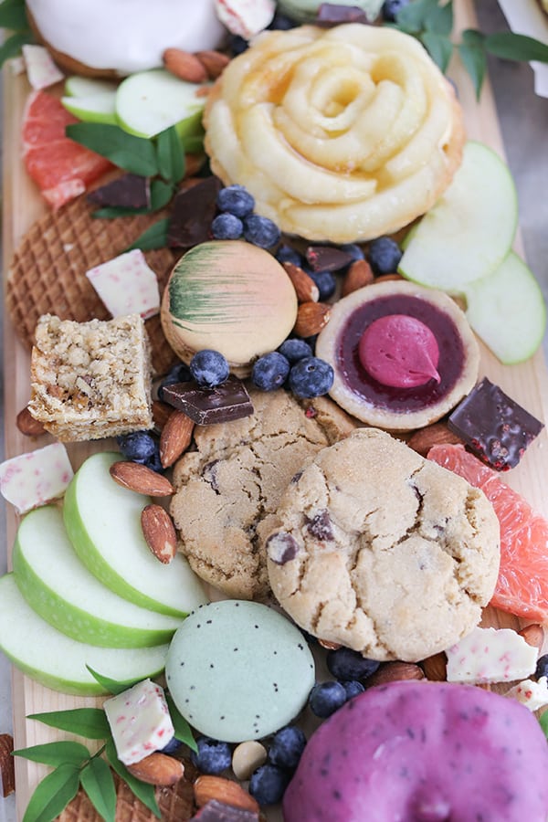 Cookies, apples, berries and bars on a wooden board.