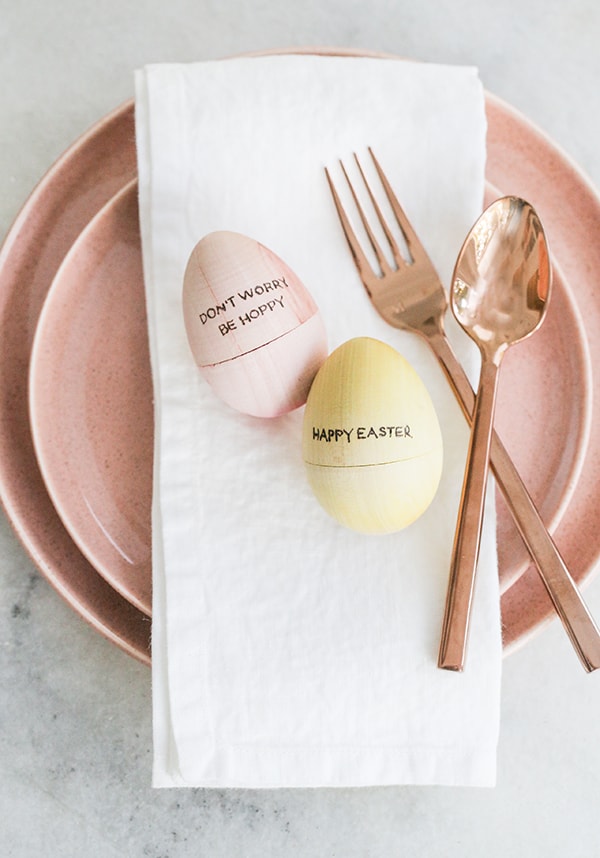 pink and yellow wooden egg with engraved letters on a pink plate with copper flatware.