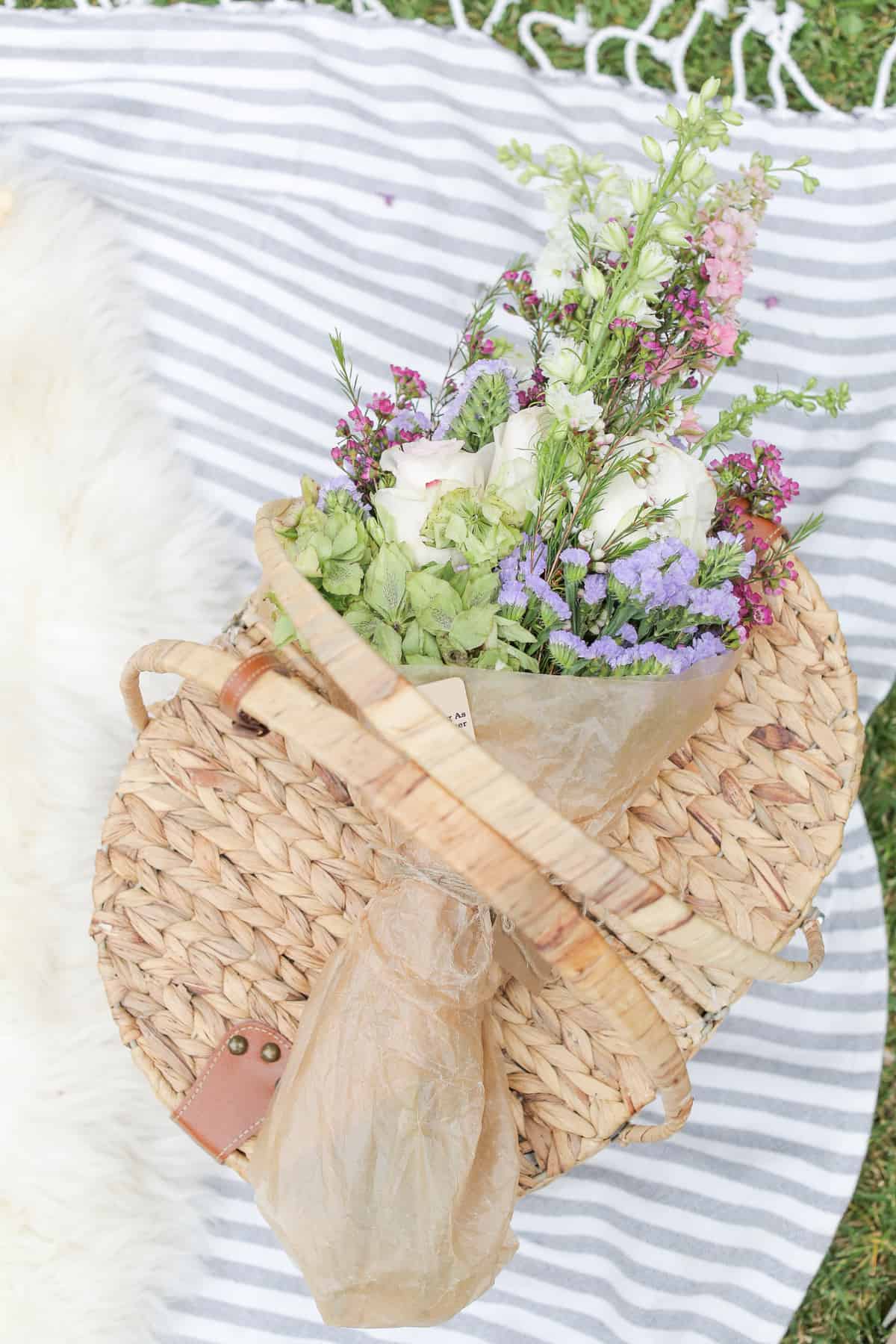 Wicker picnic basket with flowers and a picnic blanket.