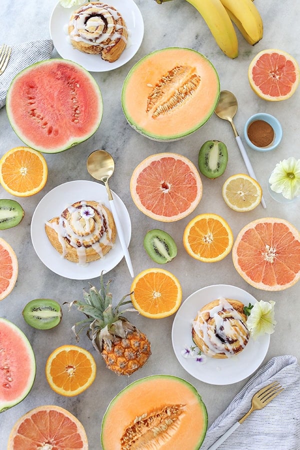 Tropical fruit sliced on a table with cinnamon rolls.