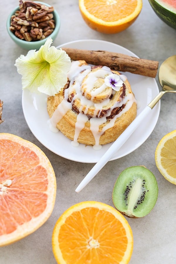 Cinnamon roll on a white plate with fruit and edible flowers.