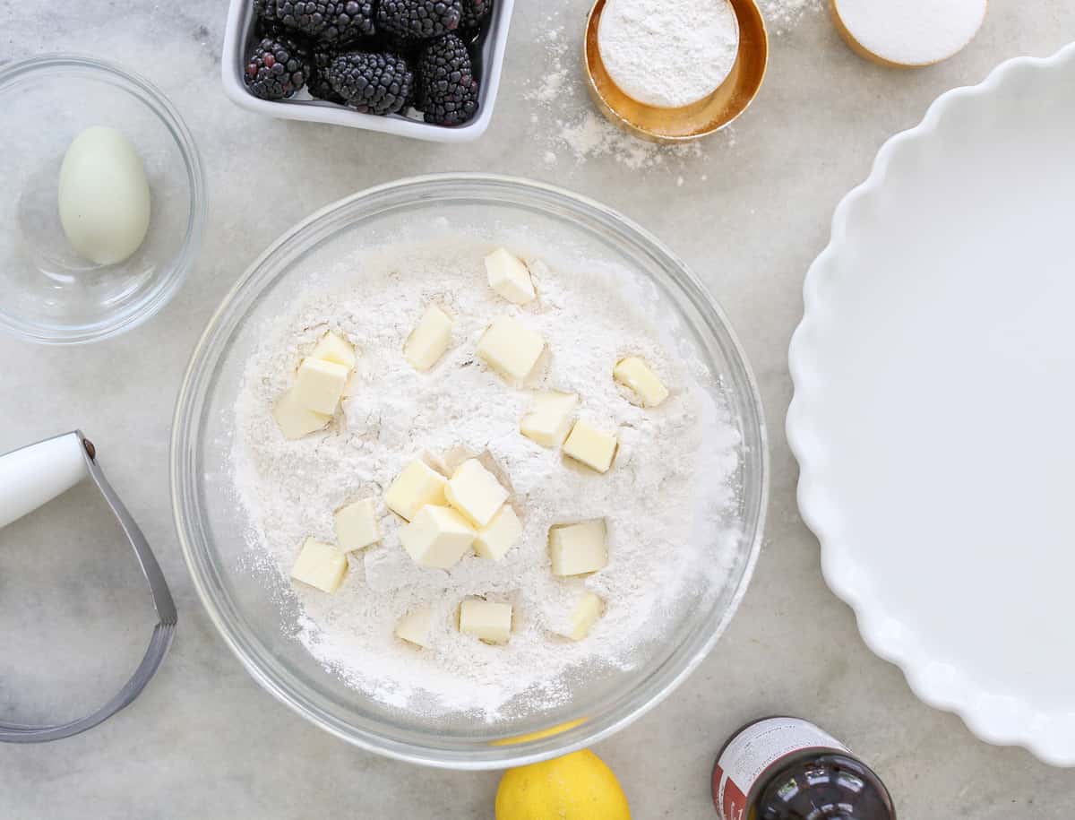 Bowl with flour, cold butter, blackberries and eggs.