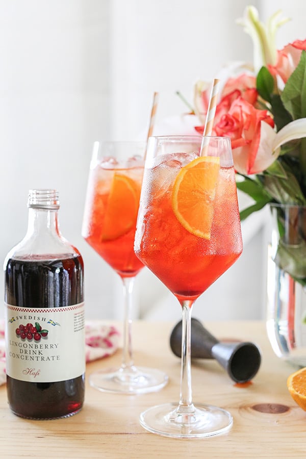 Two Aperol Spritz with Lingonberry syrup and flowers on a bar.