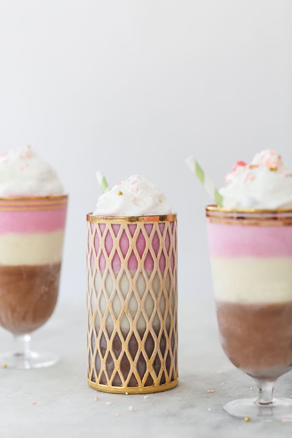 layered Neapolitan ice cream with chocolate, vanilla and strawberry milkshakes on a marble table.