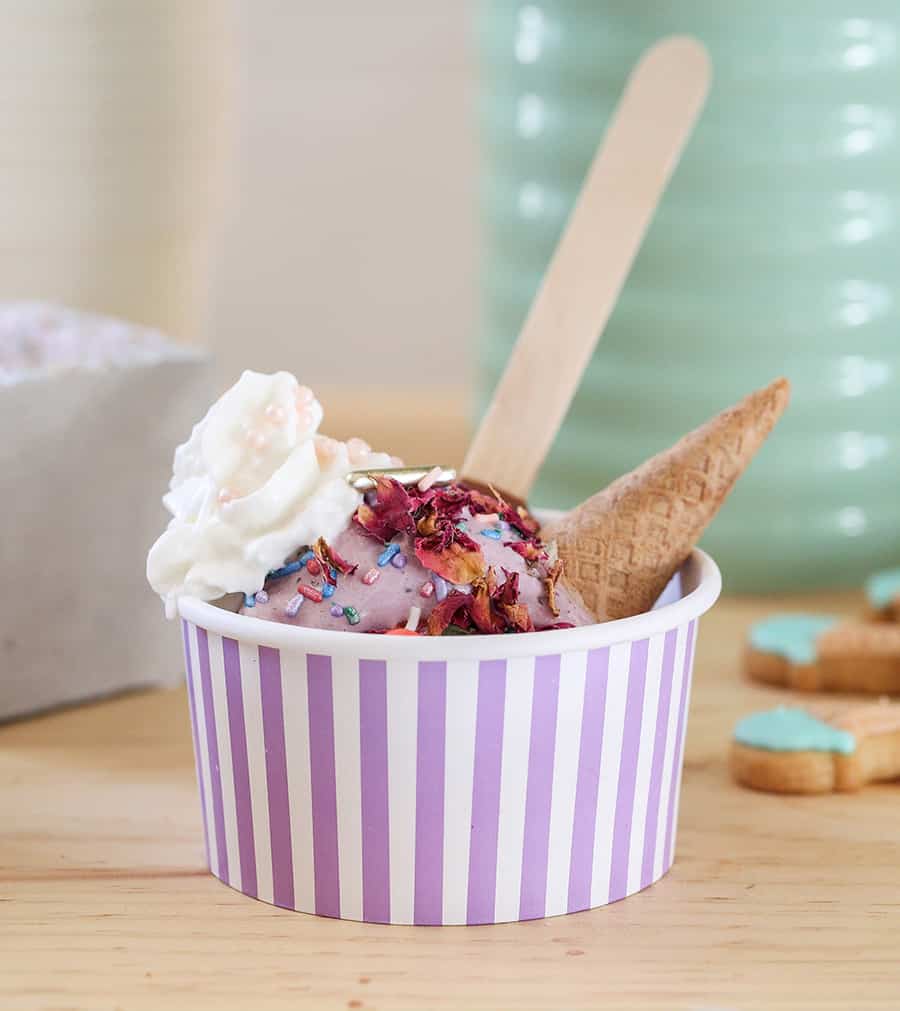 Scoop of purple ice cream with cones, flowers, whipped cream.