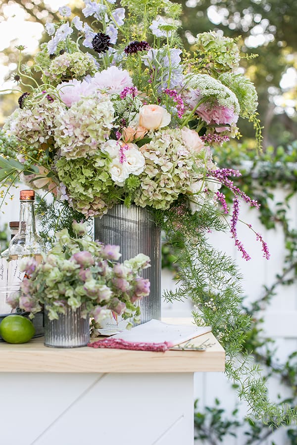 Large garden flower arrangement in a tin vase on an outdoor bar.