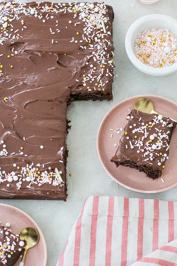 Chocolate sheet cake with sprinkles, pink plate and striped napkins.