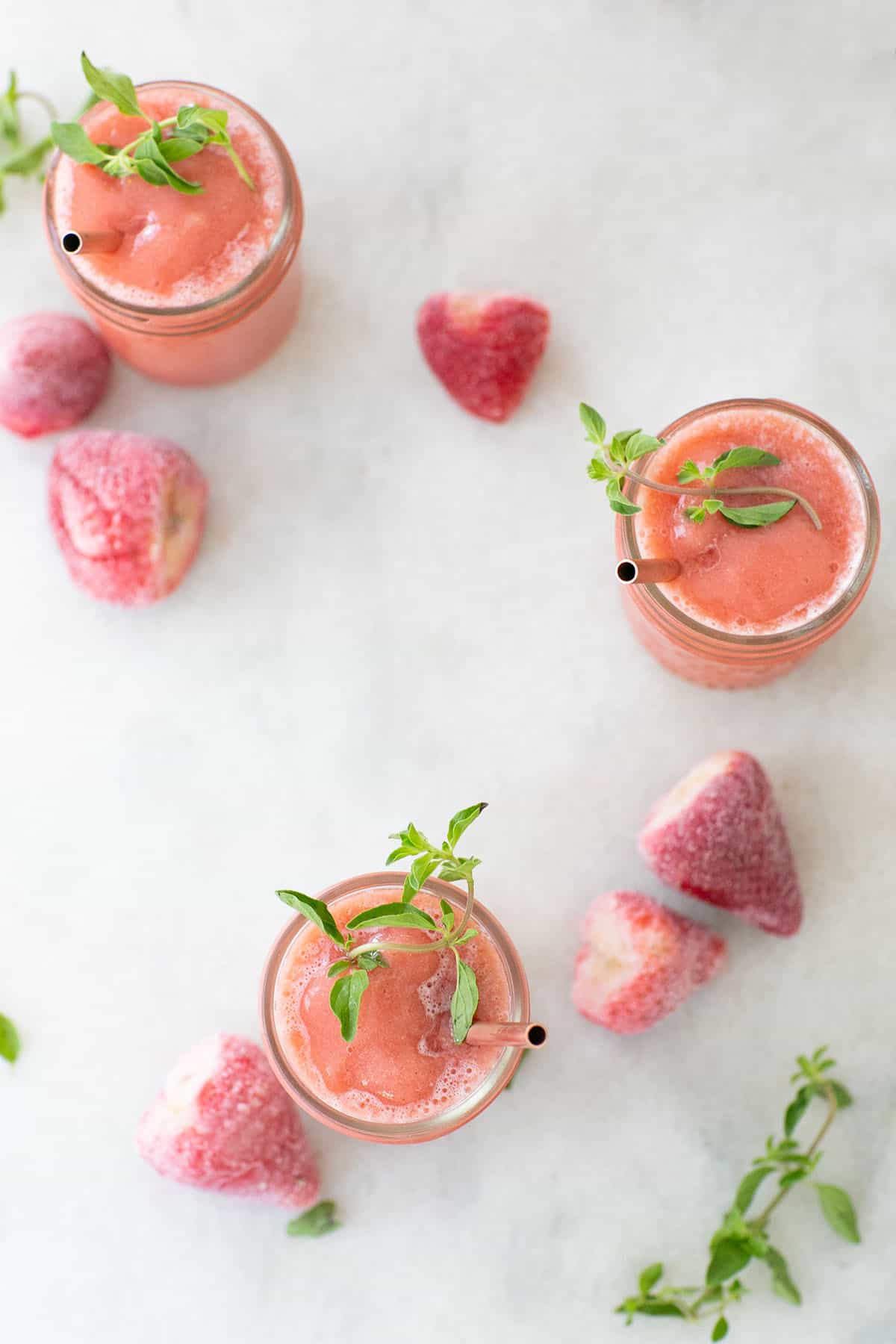 Strawberry frosé made with rosé wine served in glasses with frozen strawberries and fresh herbs.