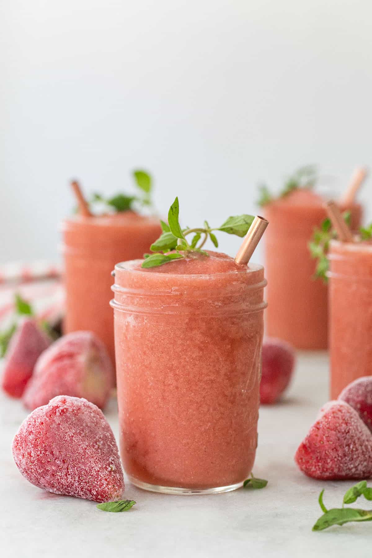 Easy frozé drink in a glass with frozen strawberries and a copper straw.