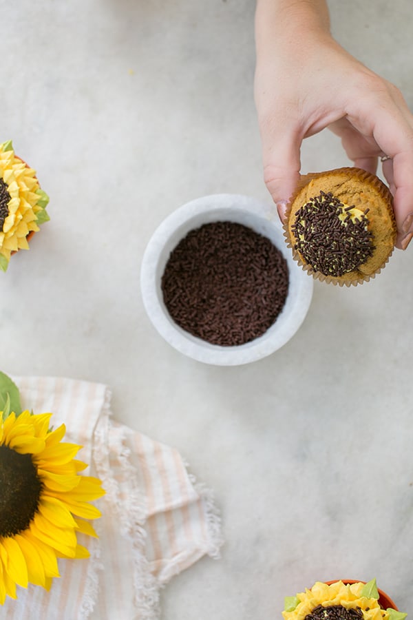 hand dipping a cupcake into bowl of chocolate sprinkles 