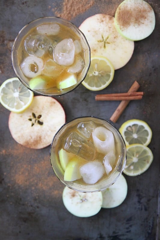 Apple cider bourbon with ice and apples on dark table.