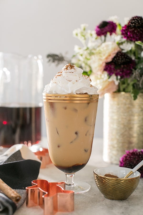 Gingerbread Cold Brew Latté with whipped cream on a table with flowers. 