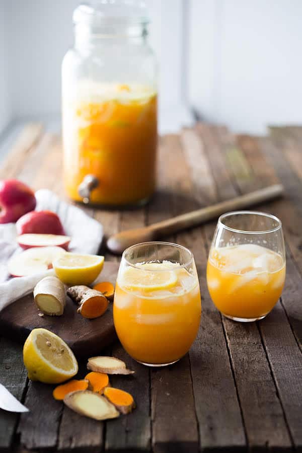 Orange turmeric ginger in glass with fresh ginger on dark wood table.