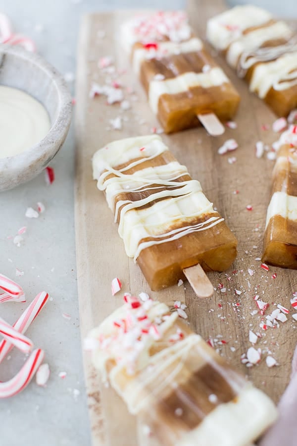 Cold brew popsicles with white chocolate on a cutting board with candy canes.