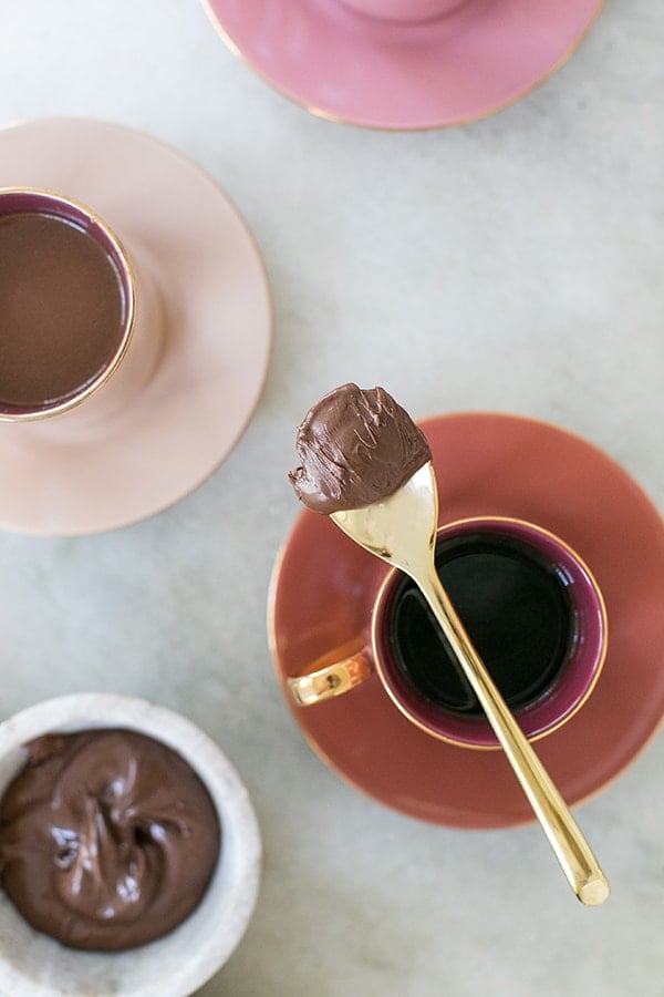 Spoon with Nutella on it over a cup of coffee.
