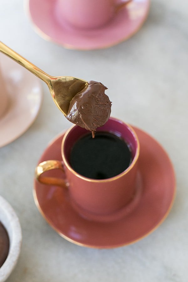 spoon with chocolate hazelnut on a gold spoon going into a cup of hazelnut coffee.