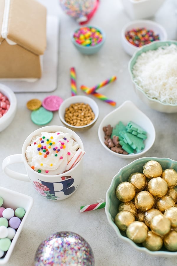 shot of hot cocoa on a table with candies around it - gingerbread house decorating party, party started