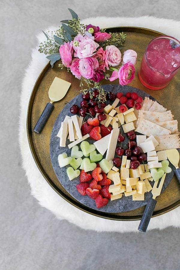 A cheese plate with heart shaped fruit and cheese on a marble board. 