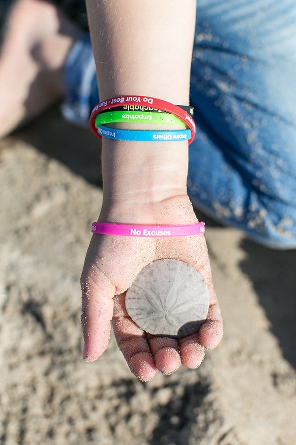 Empowering bracelets on kids hand who is holding a sand dollar. 